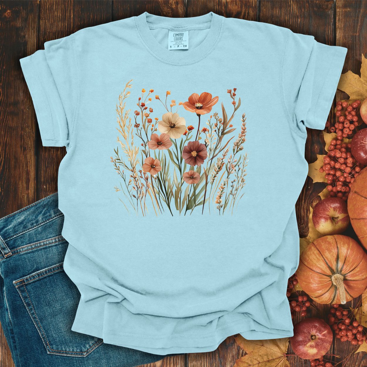 Chambray cotton t-shirt with autumn wildflowers in rust, ochre, plum, and sage, on a wooden background.