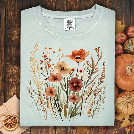 Light blue green t-shirt with autumn wildflower design on a wooden surface with pumpkins and oranges.