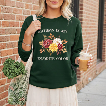 Woman in a dark green "Autumn is My Favorite Color" sweatshirt with watercolor fall flowers, holding a market bag and coffee.