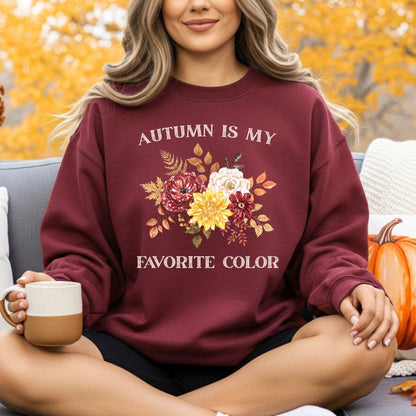 Woman wearing a maroon "Autumn Is My Favorite Color" sweatshirt with watercolor fall flowers, holding a mug.
