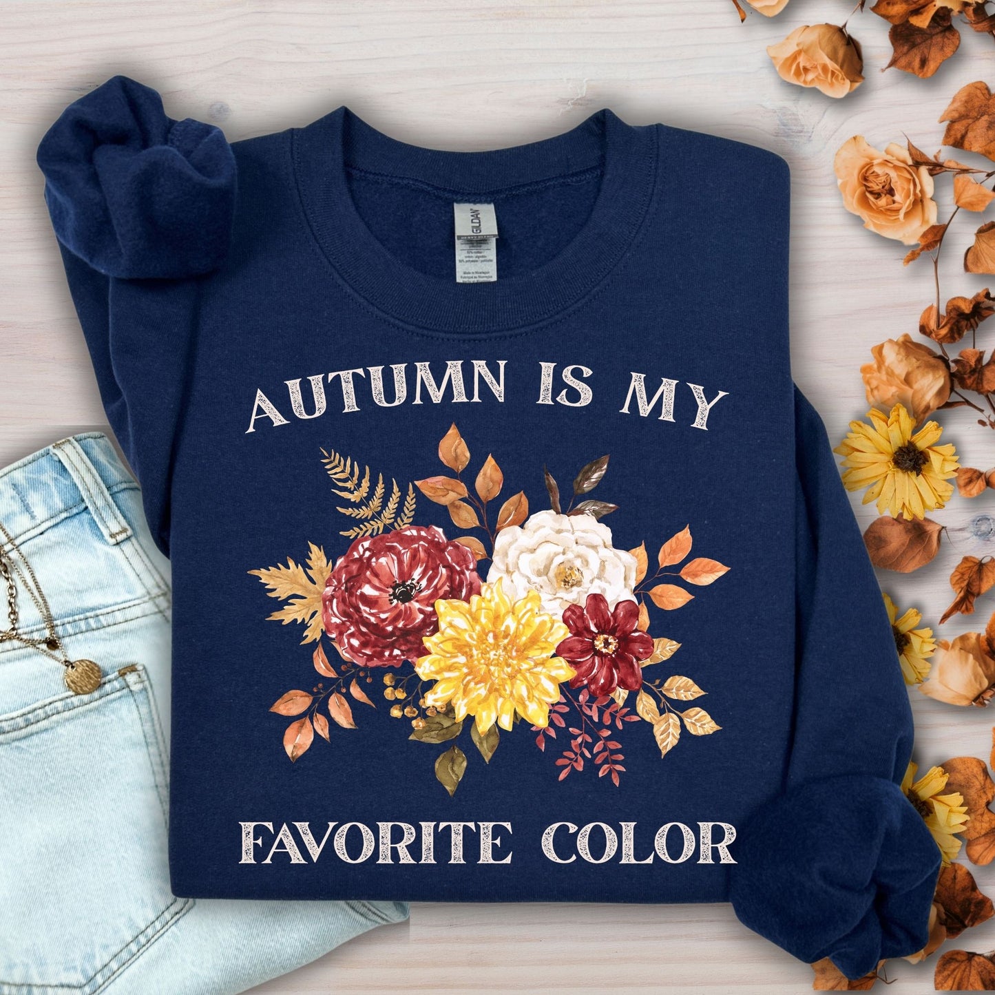 Navy 'Autumn Is My Favorite Color' sweatshirt with watercolor autumn flowers, next to jeans.