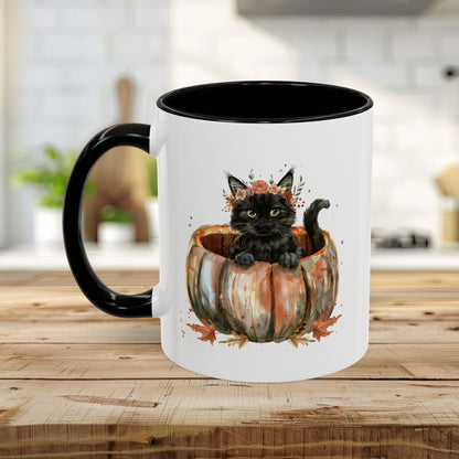 White ceramic mug with black handle and interior, featuring a watercolor black kitten in a pumpkin with autumn leaves.