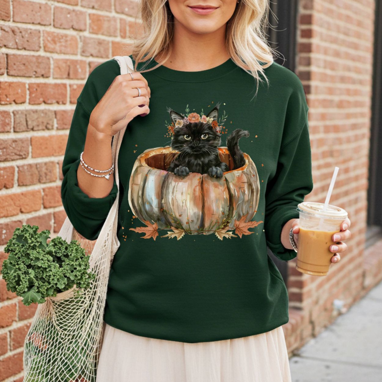 Woman in a dark green sweatshirt with a watercolor black cat in a pumpkin and fall flowers.