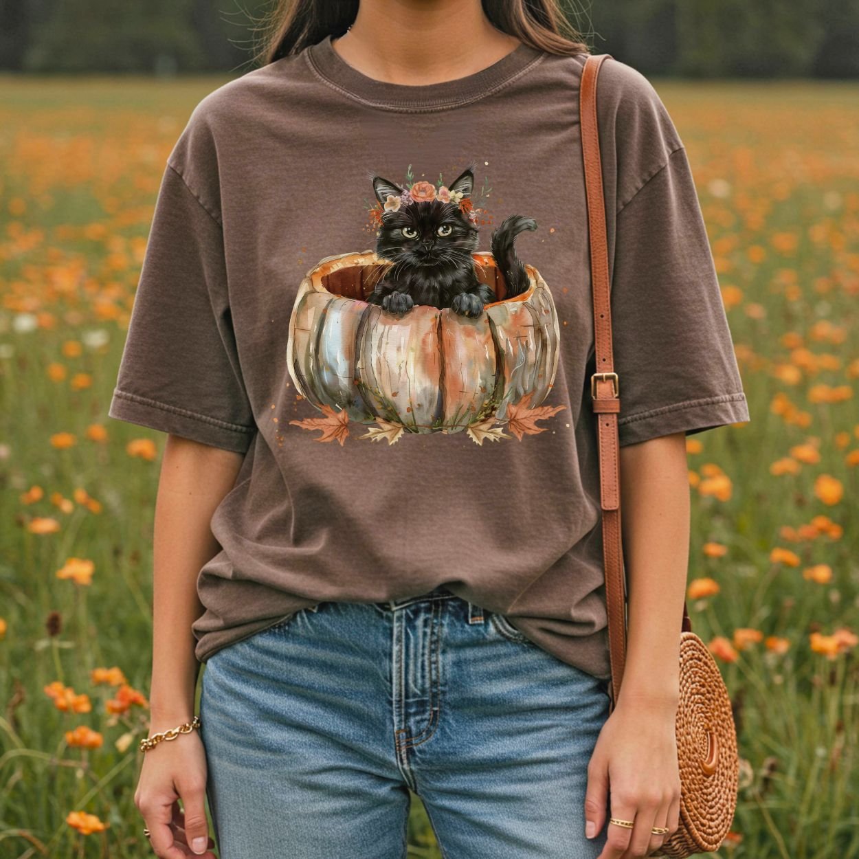 Woman in a brown Comfort Colors t-shirt with a watercolor black cat in a pumpkin and autumn flowers.