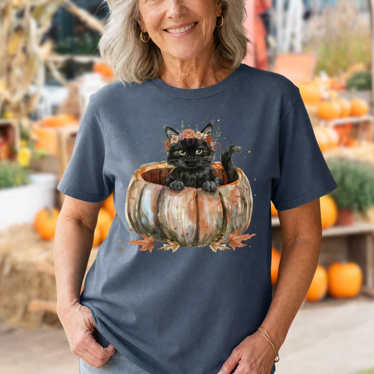 Woman in a navy Comfort Colors t-shirt with a watercolor black cat in a pumpkin and autumn flowers.