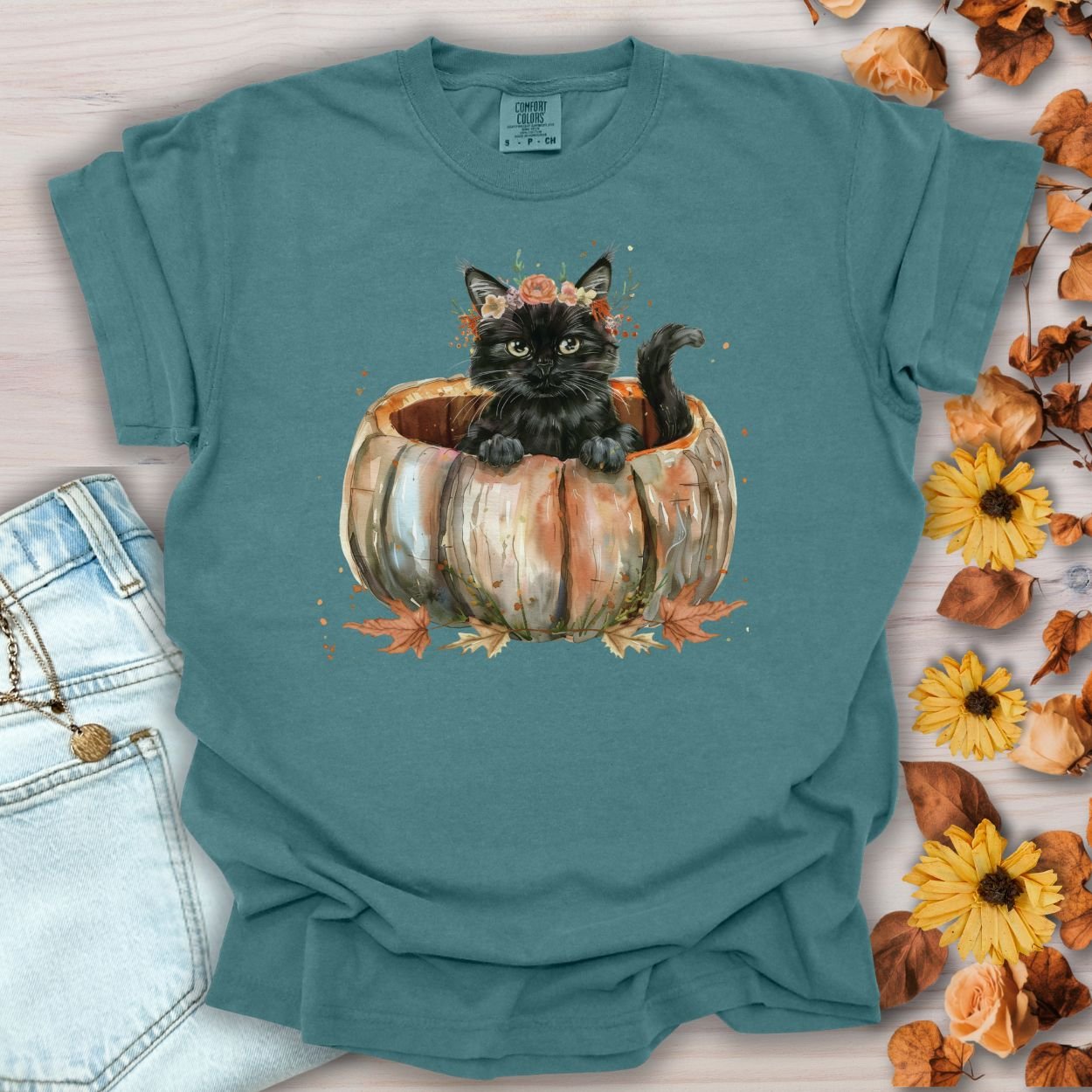Blue Spruce Comfort Colors t-shirt with a watercolor black cat in a pumpkin surrounded by autumn flowers.