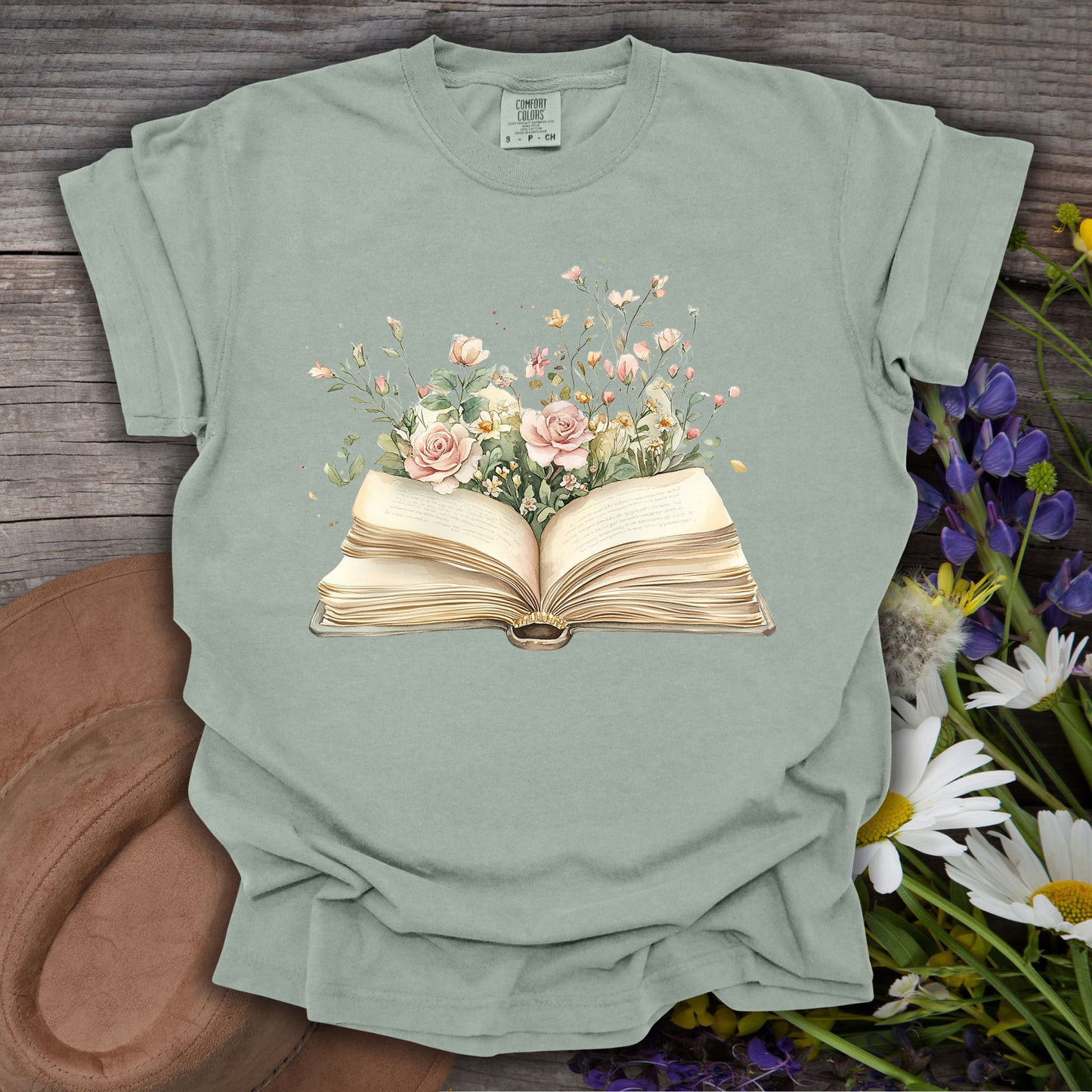 Bay S t-shirt with a watercolor illustration of an open book overflowing with pink roses and wildflowers.