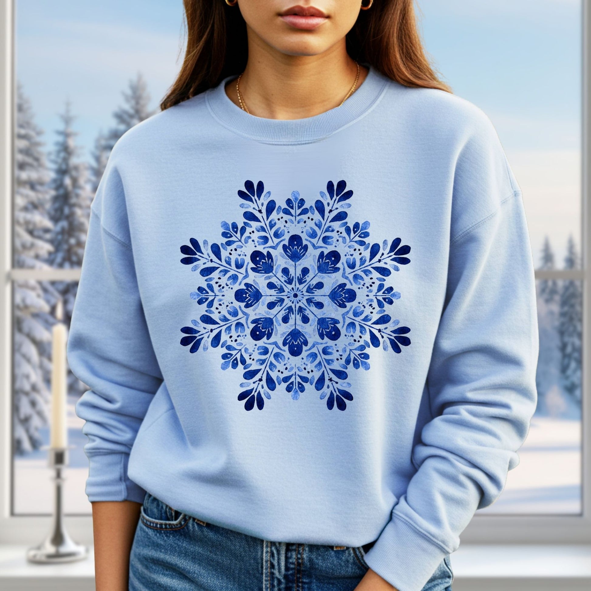 Light blue crewneck sweatshirt with a symmetrical blue floral snowflake design, worn by a person in a winter setting.