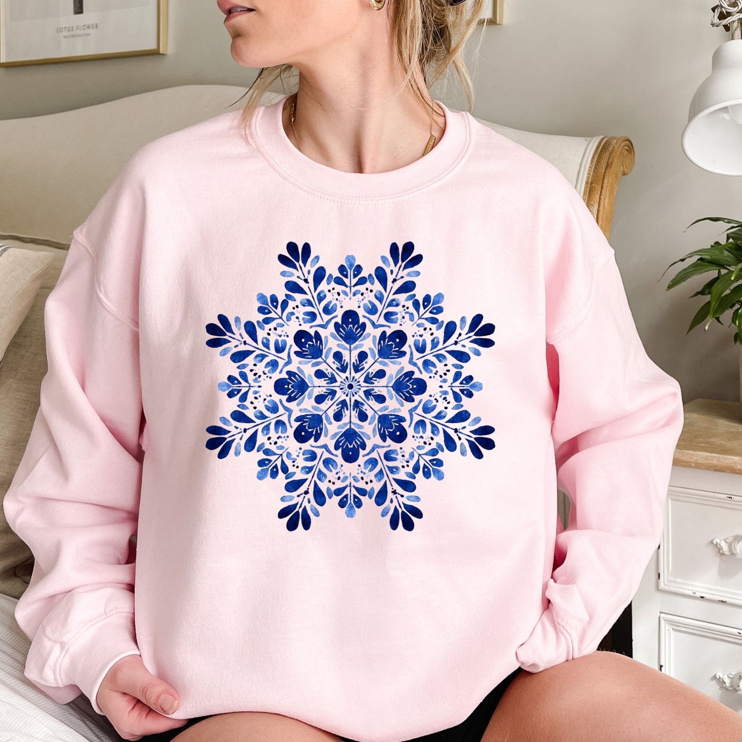 Pink crewneck sweatshirt with a large blue folk art floral snowflake design at the center.