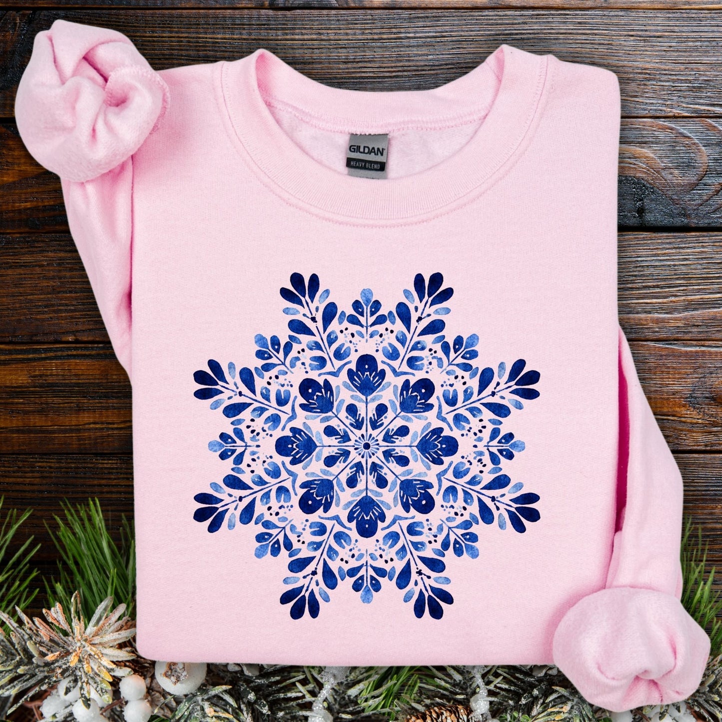 Light pink crewneck sweatshirt with a blue folk art snowflake design, made from ethically sourced cotton.