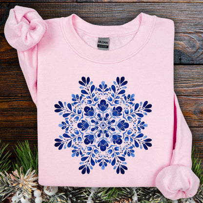 Light pink crewneck sweatshirt with a blue folk art snowflake design, made from ethically sourced cotton.