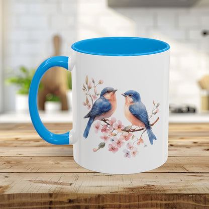 White ceramic mug with blue interior and handle, featuring watercolor bluebirds on cherry blossoms.