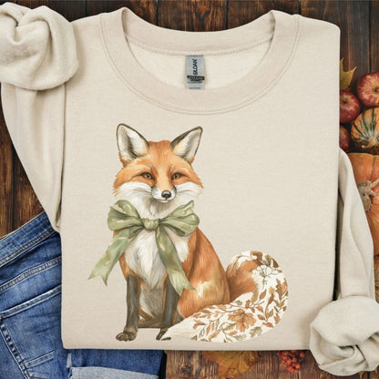Sand Gildan sweatshirt with a fox wearing a green bow and fall botanicals on its tail.