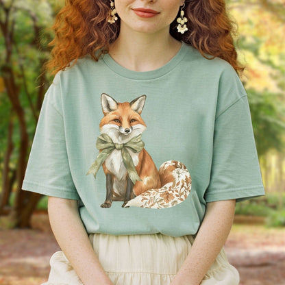 Garment-dyed sage green t-shirt with a watercolor fox wearing a green bow and a leaf-patterned tail.