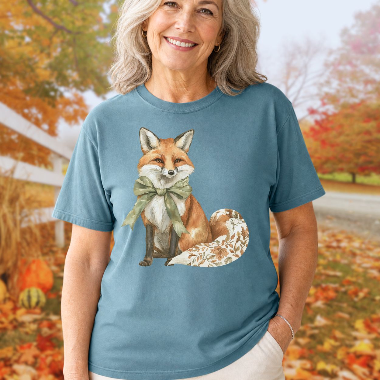 Garment-dyed blue t-shirt with a watercolor fox wearing a sage-green bow and a leaf-patterned tail.