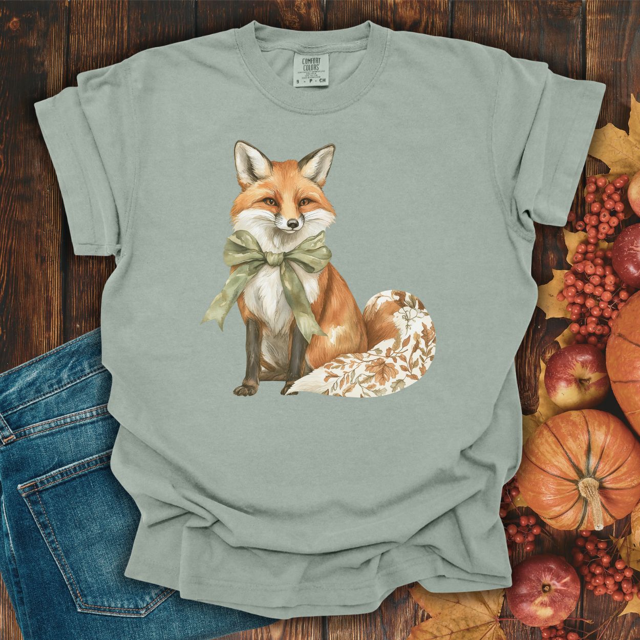 Bay S garment-dyed t-shirt with a watercolor fox wearing a sage-green bow and a leaf-patterned tail.