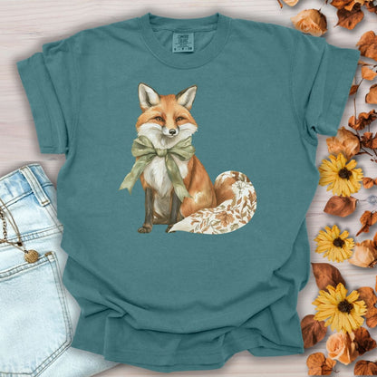 Blue Spruce S t-shirt with a watercolor fox wearing a sage-green bow and a leaf-patterned tail.