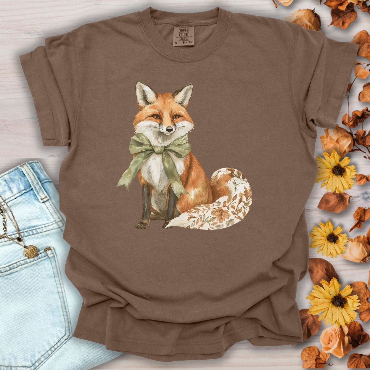 Espresso garment-dyed t-shirt with a watercolor fox wearing a sage-green bow and a leaf-patterned tail.