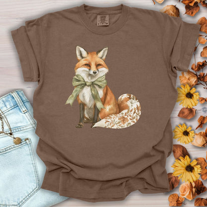Espresso garment-dyed t-shirt with a watercolor fox wearing a sage-green bow and a leaf-patterned tail.