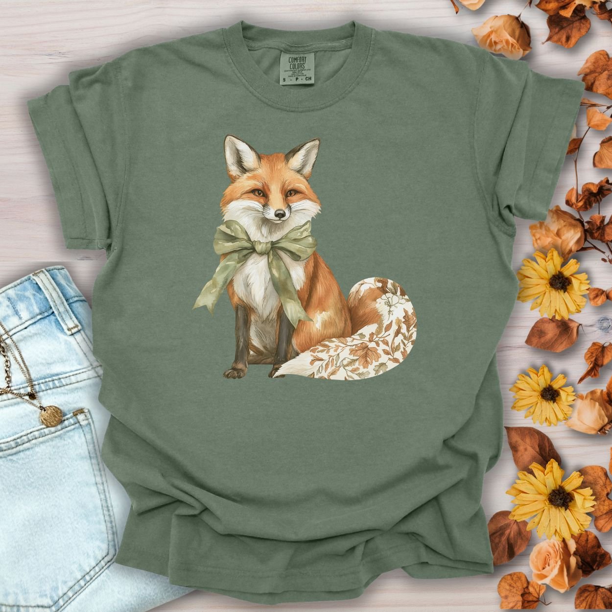 Moss green garment-dyed t-shirt with a watercolor fox wearing a sage green bow and a leaf-patterned tail.