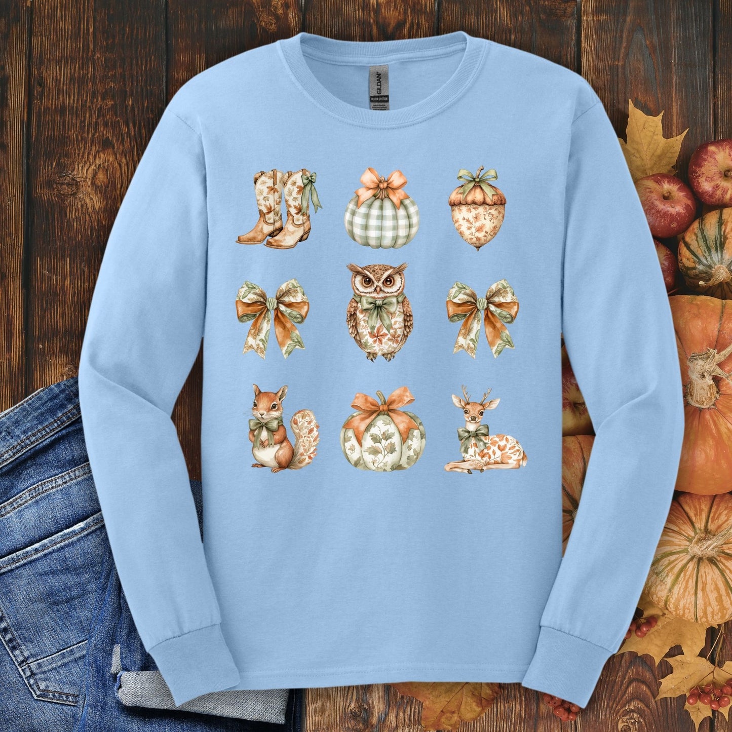 Light blue long sleeve tee with cottagecore fall design: owl, boots, acorn, squirrel, deer, pumpkins, and bows.