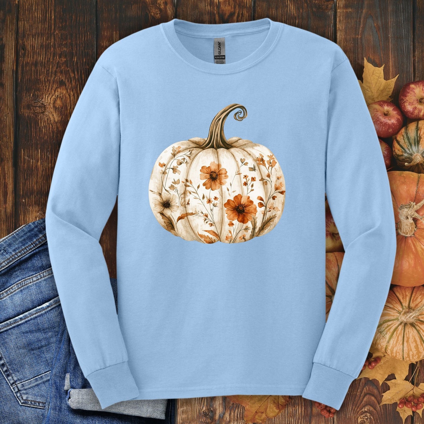 Light blue long sleeve tee with a white boho floral pumpkin design, surrounded by fall leaves and apples.