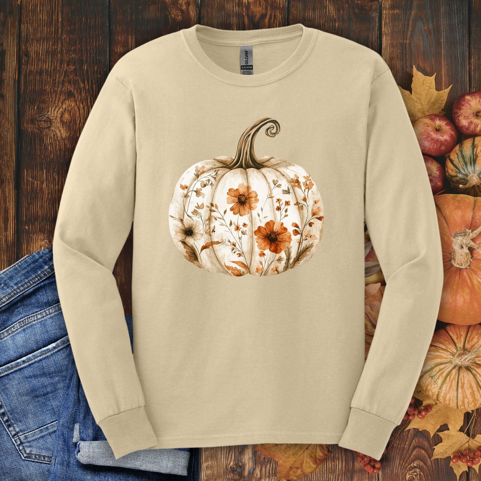 Sand Gildan long sleeve tee with a white boho floral pumpkin design, surrounded by fall leaves and small pumpkins.