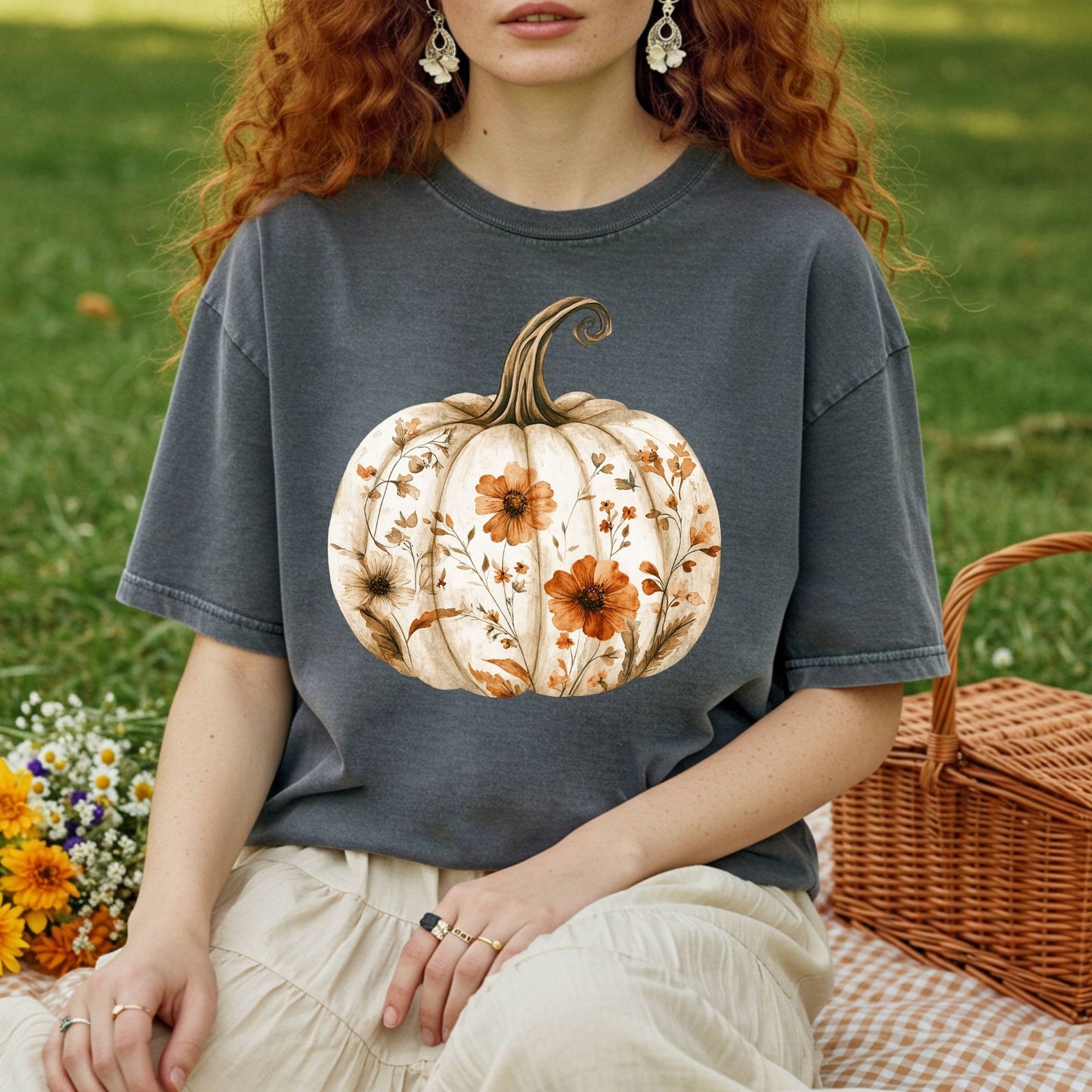 Garment-dyed charcoal t-shirt with a white pumpkin blooming with delicate wildflowers, worn by a person on a picnic blanket.