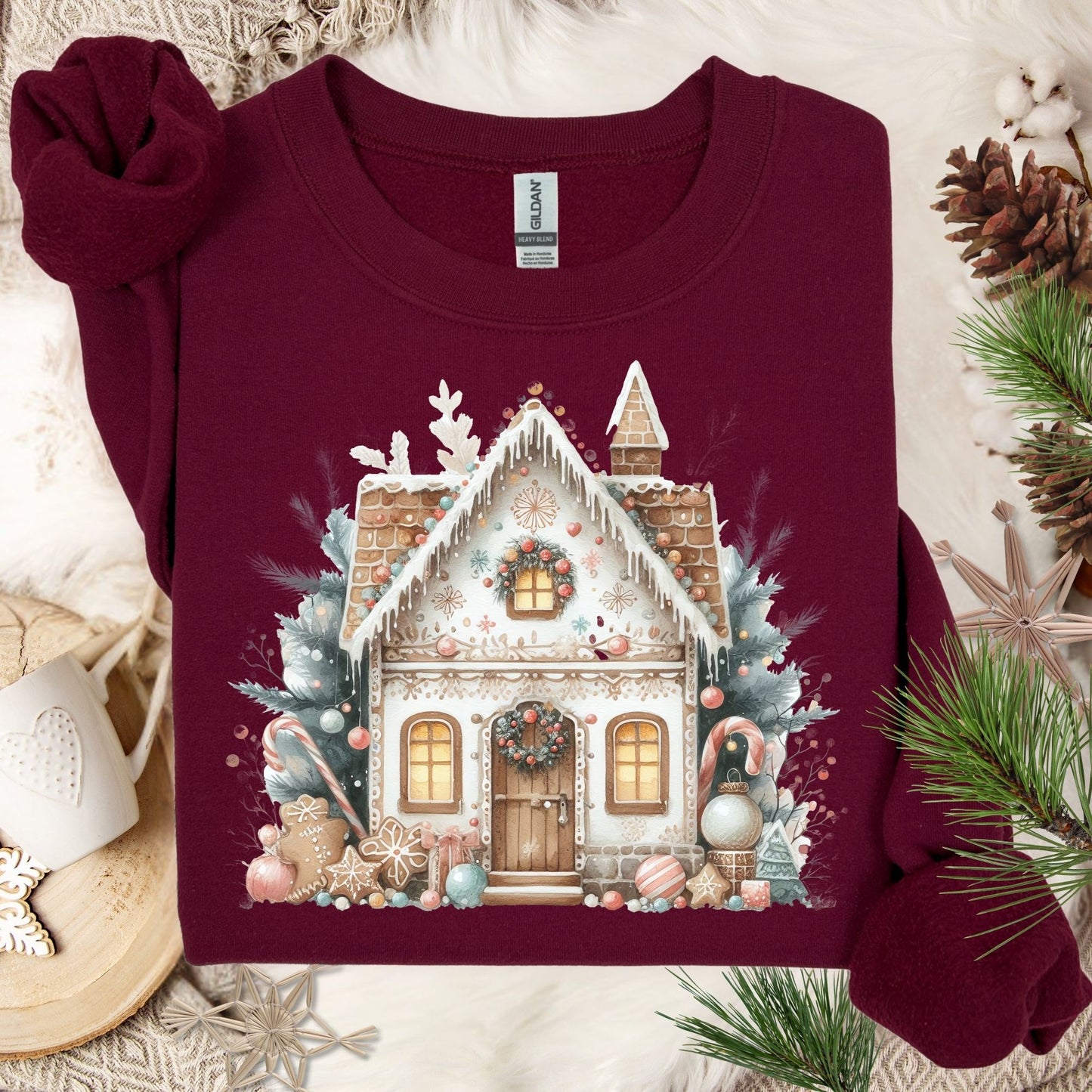 Maroon Gildan crewneck sweatshirt with a watercolor boho gingerbread house design, surrounded by festive decor.