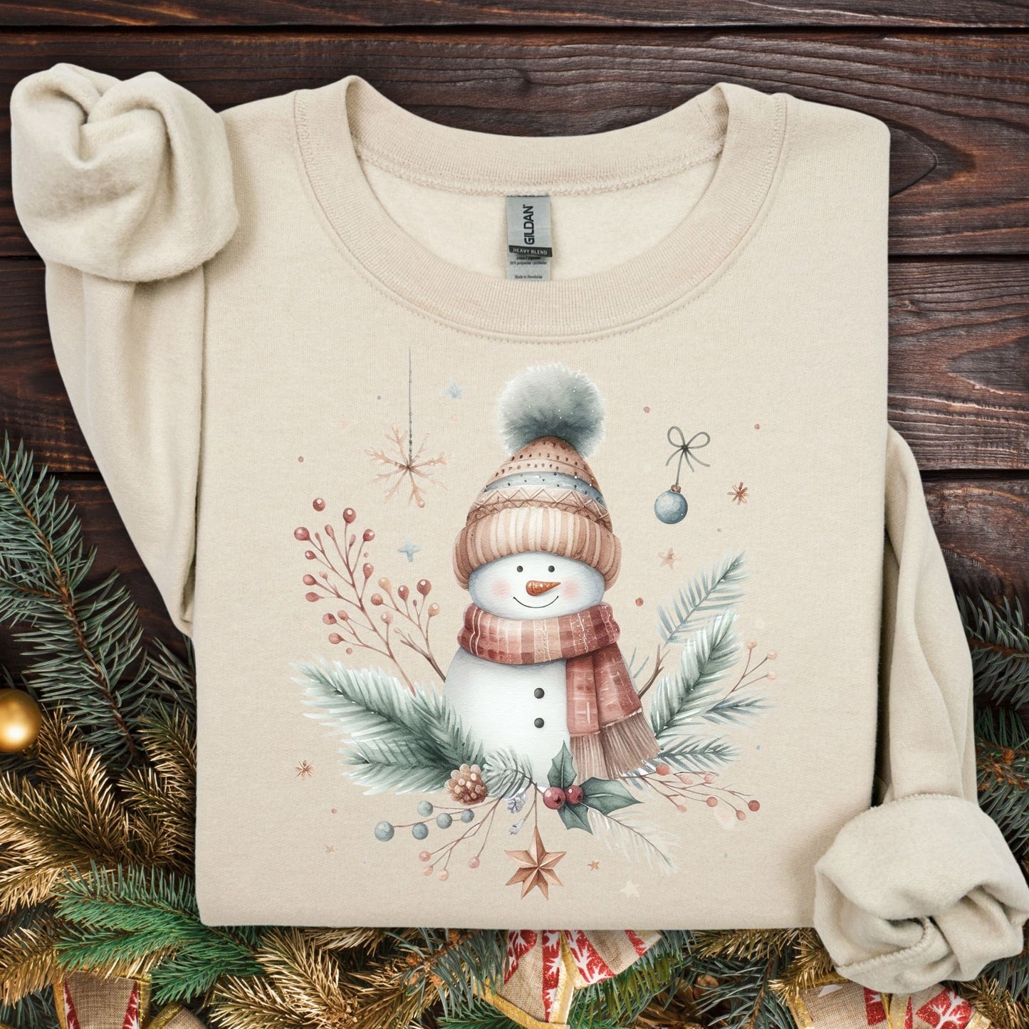 Sand crewneck sweatshirt with a boho watercolor snowman in a flannel scarf and hat, surrounded by evergreens.