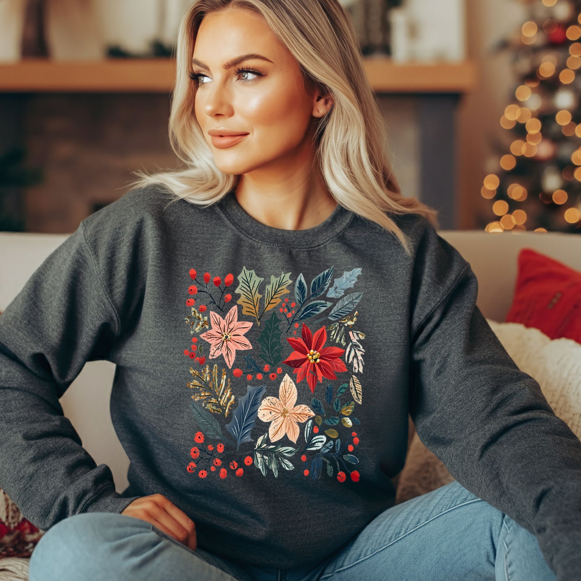Blonde woman in a charcoal long sleeve tee with a vibrant boho poinsettia floral design, sitting on a couch.