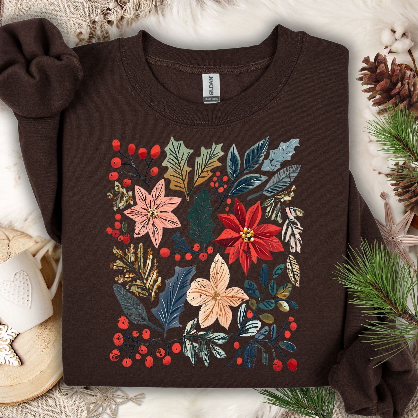 Dark chocolate Gildan sweatshirt with vibrant boho watercolor poinsettias, leaves, and berries, surrounded by festive decor.