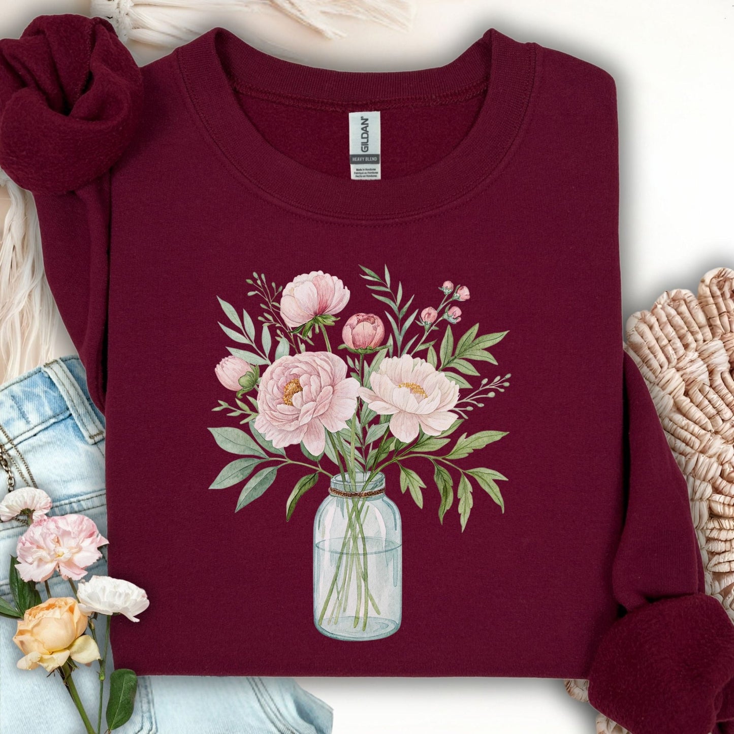 Maroon sweatshirt with a botanical illustration of pink peonies in a glass jar.