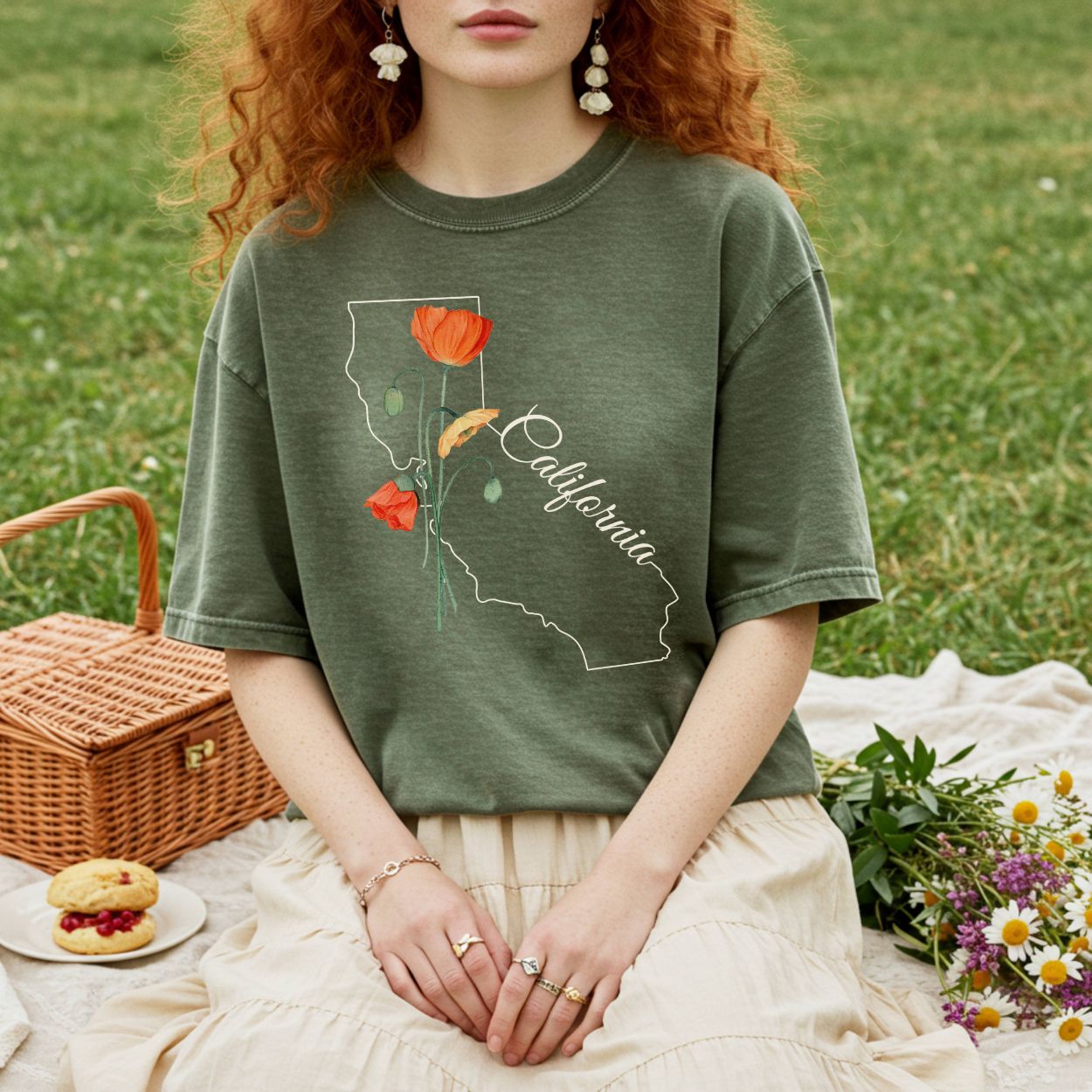 Garment-dyed, relaxed-fit olive green t-shirt with a California map and poppy design, worn by a person on a picnic blanket.