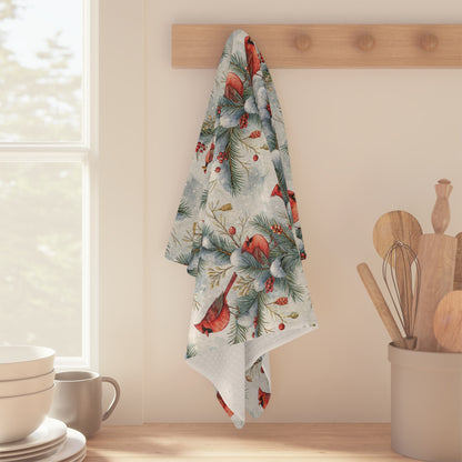 Microfiber tea towel with watercolor cardinals, snowy pine, and holly berries, hanging on a wooden peg.