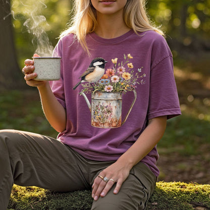 Garment-dyed plum t-shirt with a chickadee perched on a watering can full of wildflowers.