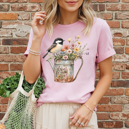 Pink garment-dyed t-shirt with a chickadee perched on a floral watering can, worn by a woman holding kale.