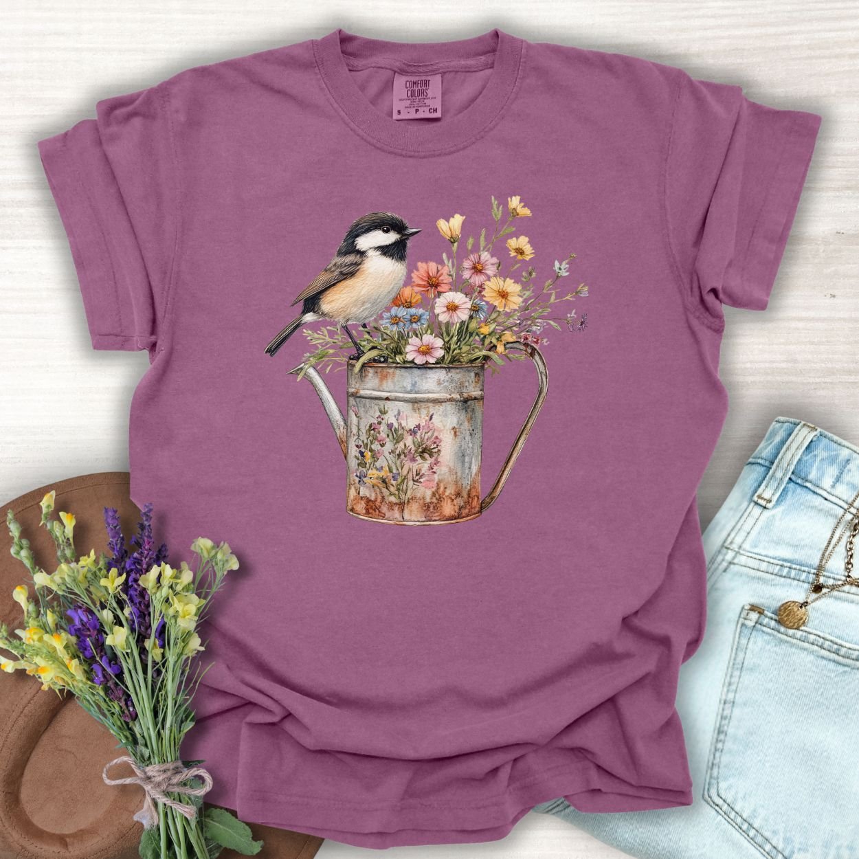 Berry S t-shirt with a chickadee perched on a weathered watering can brimming with wildflowers.