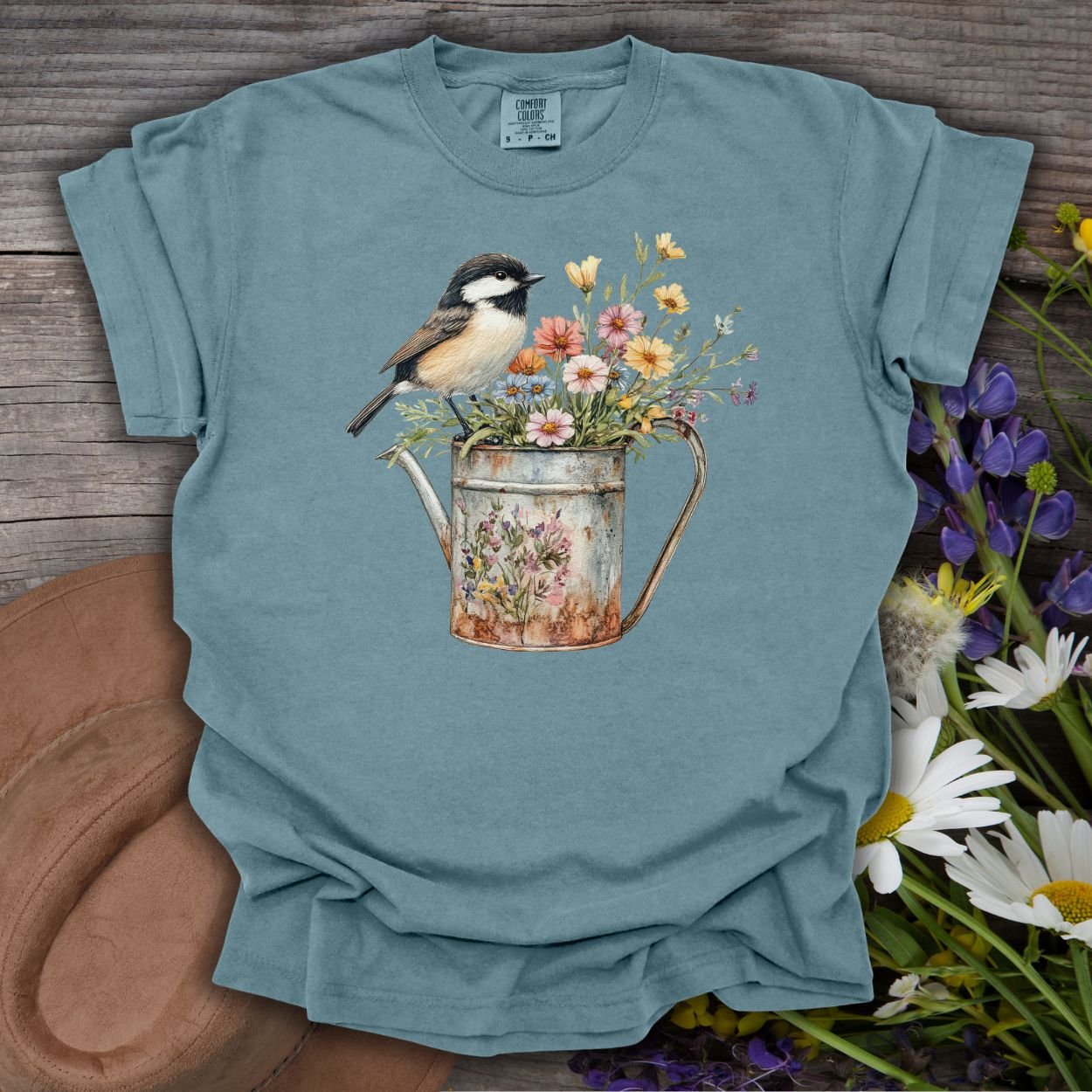 Ice Blue S t-shirt with a chickadee perched on a floral watering can, on a rustic wood background.