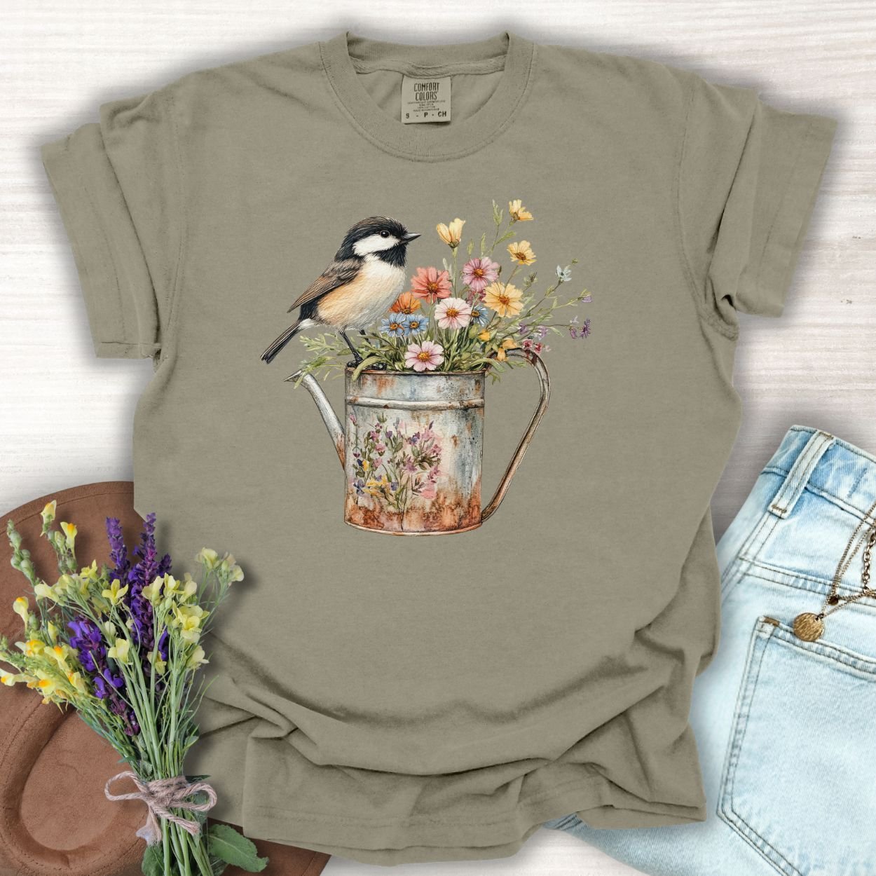 Khaki garment-dyed cotton t-shirt with a chickadee perched on a floral watering can design.