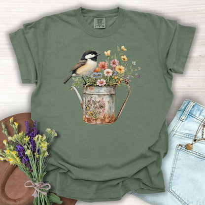 Moss green garment-dyed tee with a chickadee perched on a rustic watering can filled with wildflowers.