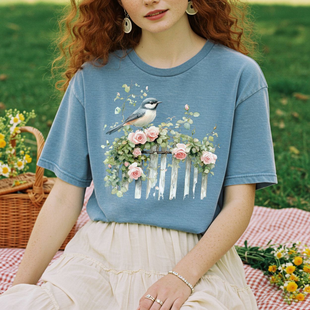 Garment-dyed blue t-shirt with a watercolor chickadee on a rose-covered white picket fence.