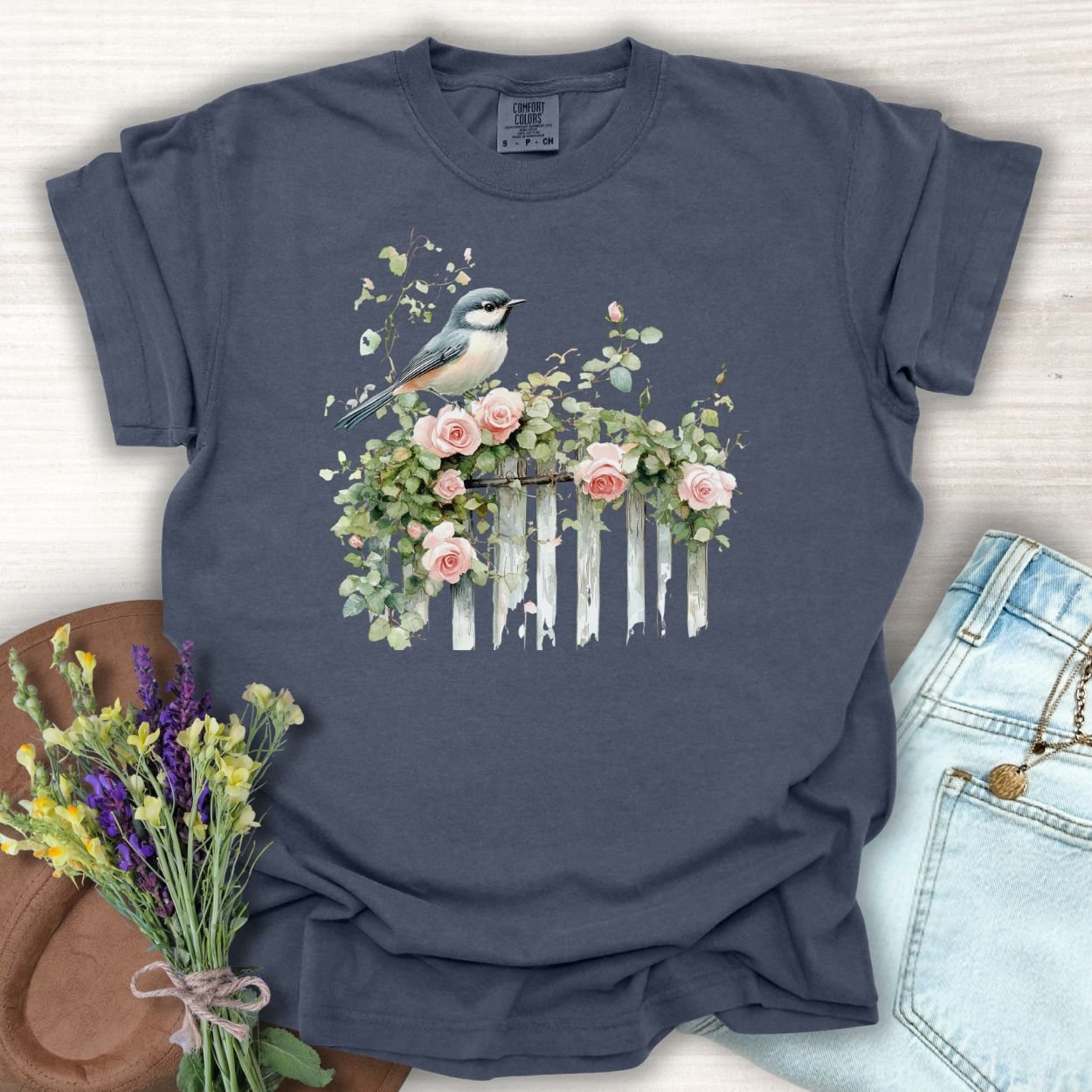 Denim blue garment-dyed t-shirt with a watercolor chickadee on a rose-covered fence.