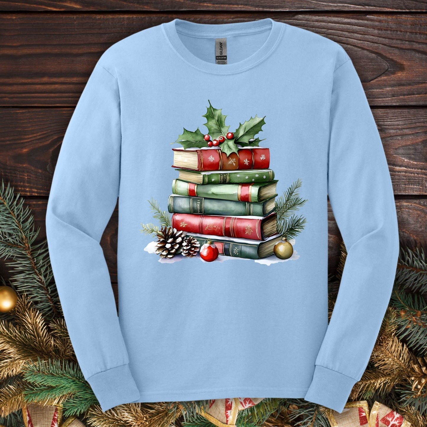 Light blue long sleeve tee with a vintage watercolor Christmas book stack, holly, pinecones, and ornaments.