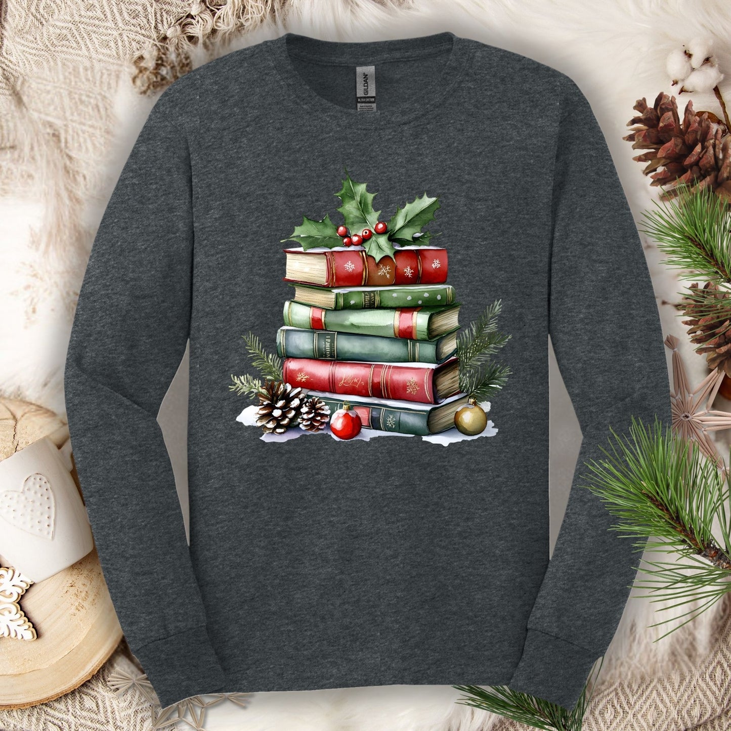 Dark heather long sleeve tee with a watercolor Christmas book stack, holly, pinecones, and ornaments.
