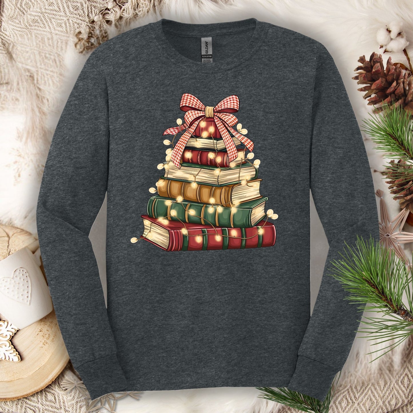 Dark Heather long sleeve tee with a watercolor stack of vintage Christmas books forming a tree, adorned with a red gingham bow and string lights.