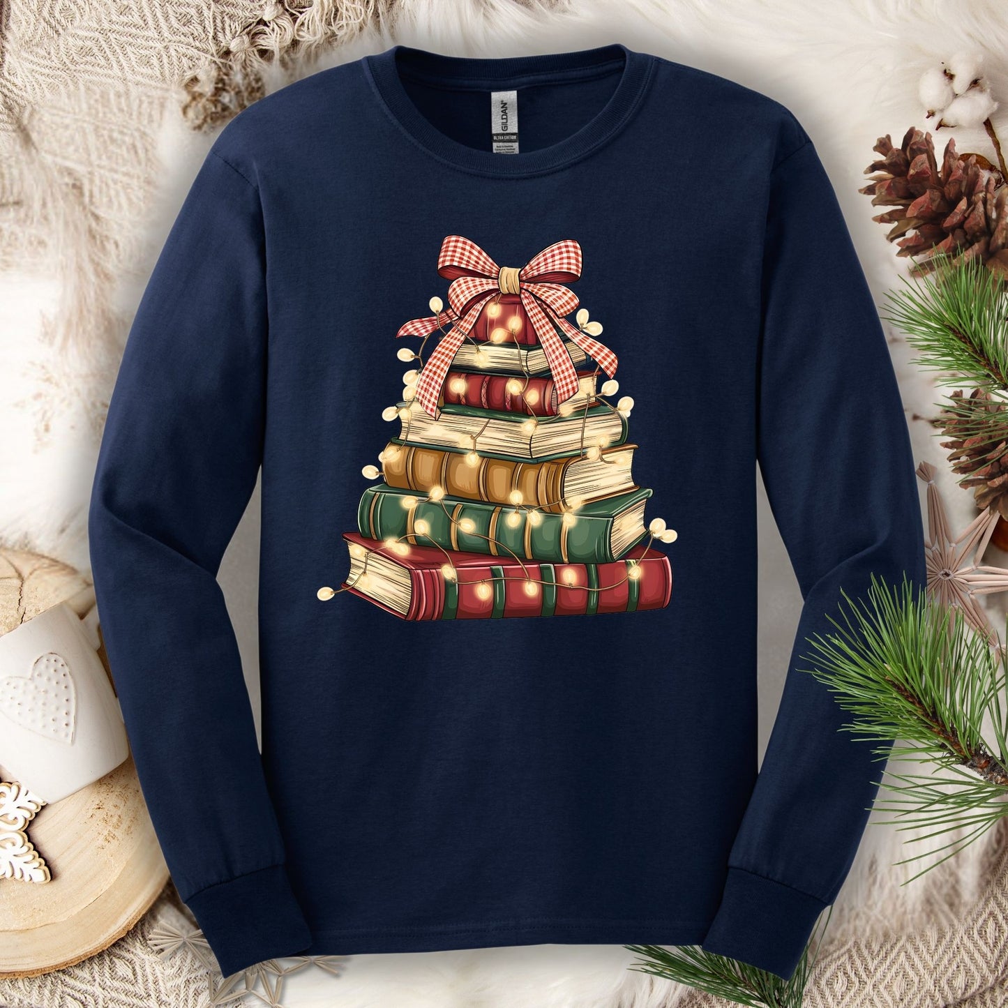 Navy long sleeve tee with a watercolor Christmas book tree design, topped with a plaid bow and string lights.