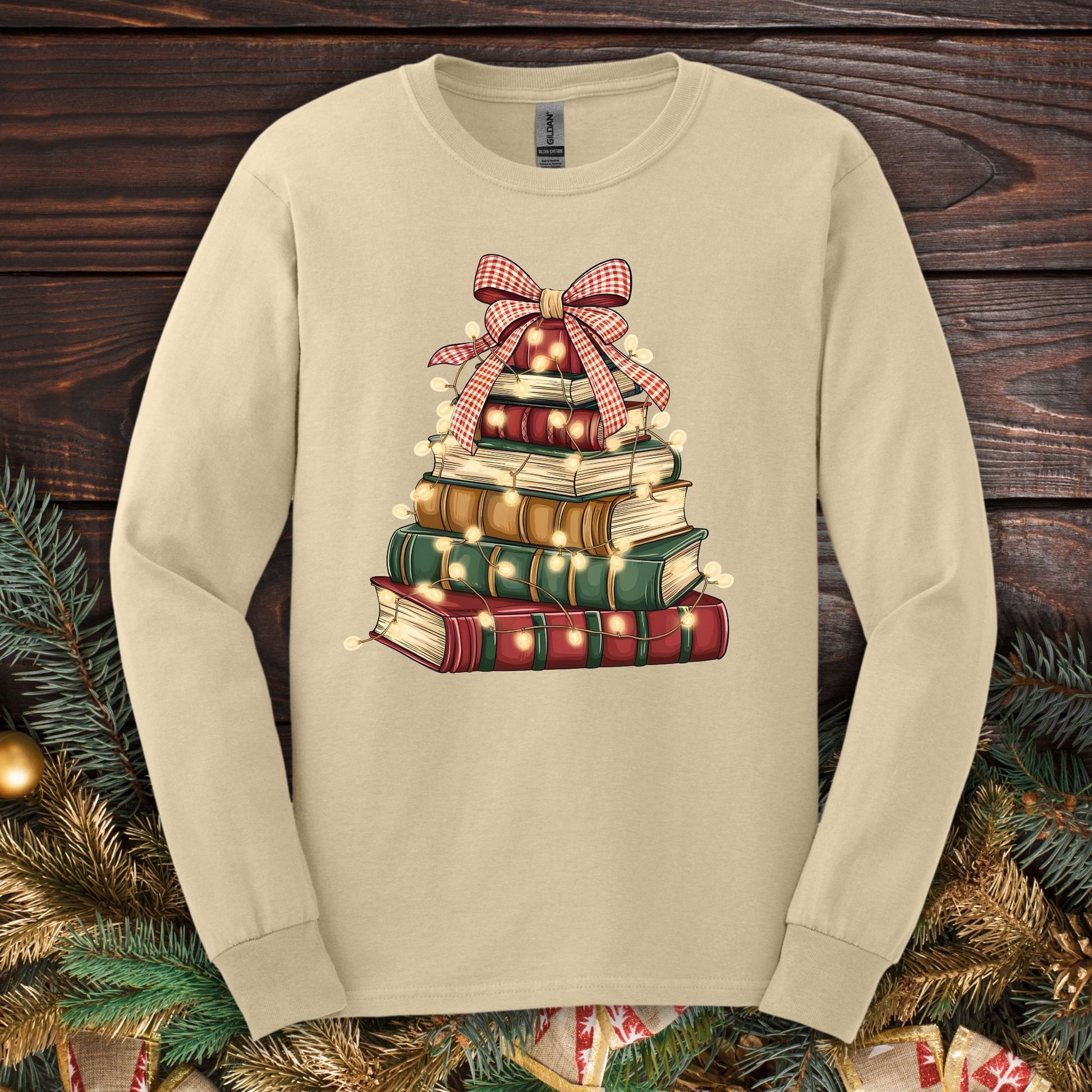 Sand long sleeve tee with a watercolor Christmas book tree design, festive bow, and string lights.
