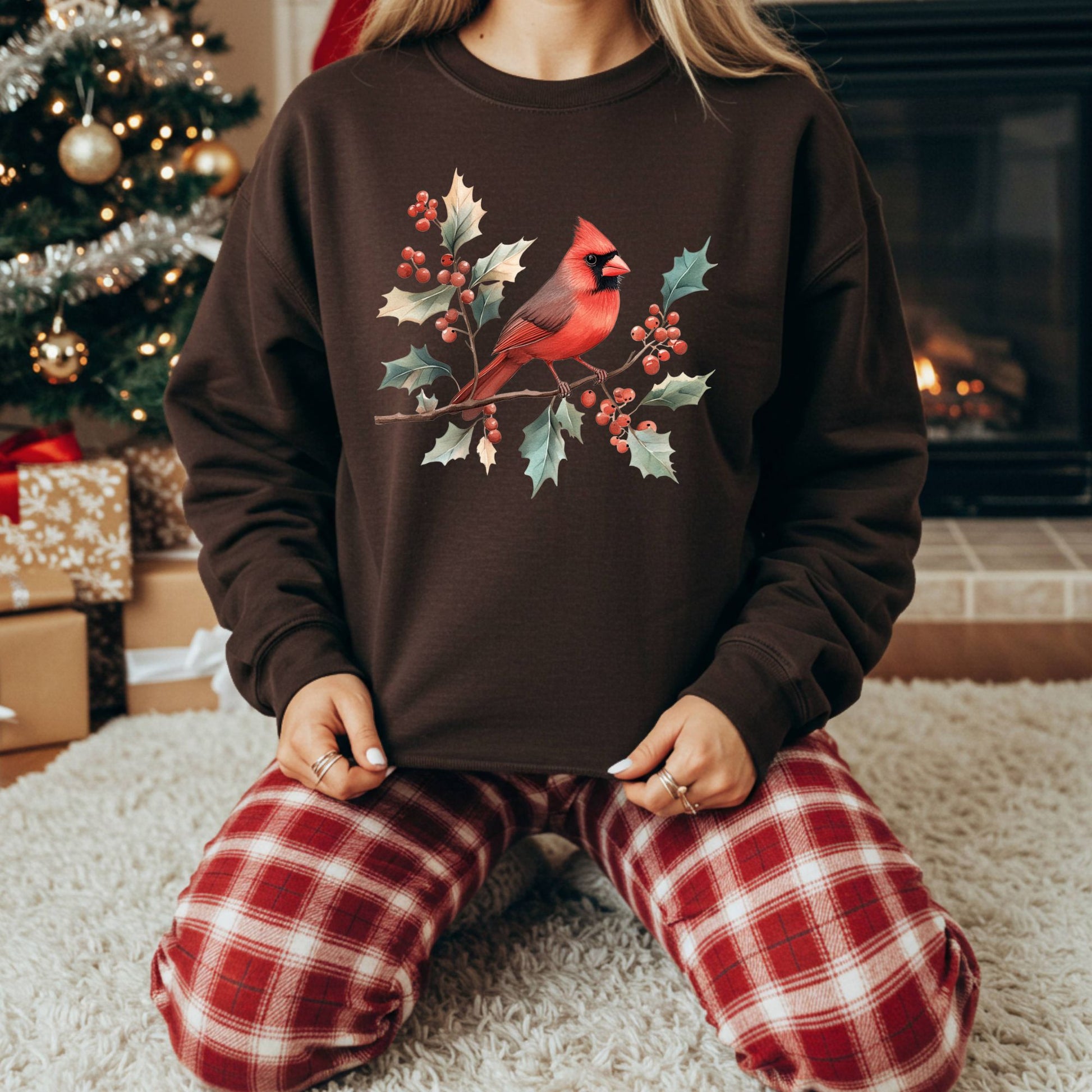 Brown crewneck sweatshirt with a vibrant cardinal and holly branch design, worn by a person in plaid pajamas.