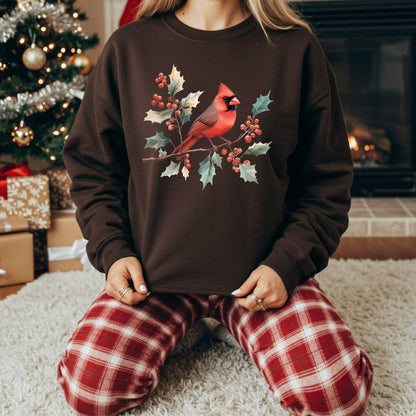 Brown crewneck sweatshirt with a vibrant cardinal and holly branch design, worn by a person in plaid pajamas.